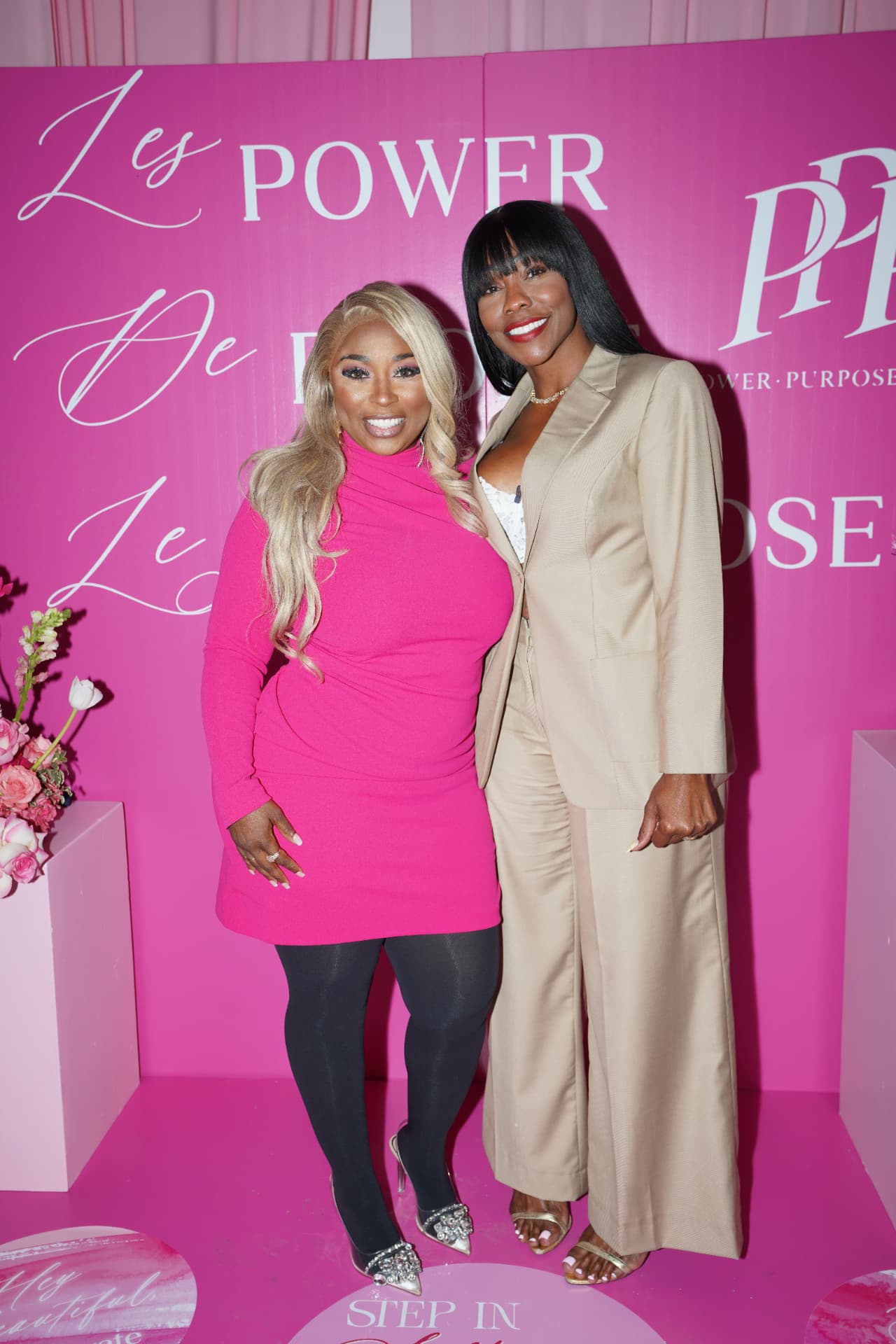 Two hosts standing in front of the pink Power Purpose Profit backdrop
